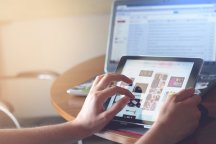 Osoba koja sjedi uz računar također u rukama drži tablet na kojemu pretraživa na internetu slike